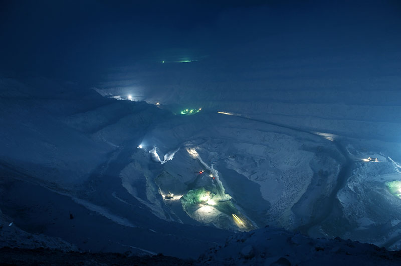 Norilsk se situe sur le plateau de Sibérie occidentale et au pied des montagnes de Putoran, culminant à 1700 mètres d'altitude. Norilsk possède les plus importants gisements de nickel, de cuivre et de palladium dans le monde. Ce dépôt a été formé il y a environ 250 millions d'années lors de la formation de la Sibérie. Aujourd'hui, l’entreprise de Norisk « Norilsk Nickel » est devenu le premier producteur mondial de palladium, minerais représentant 40% de la production du combinat. Avec 36% de la production mondiale, Norilsk se retrouve aussi au premier plan de la production de platine. Ces production assure près de 2% du PIB russe : janvier 2001, le palladium se négociait à plus de 1 000 dollars de l'once et à 480 dollars l'once en avril 2008. Le Nickel s’adjuge lui à 25 000 dollar la tonne. En 2007, Norilsk Nickel, qui contribue à 90% du budget de la ville, a produit : - plus de 300 000 tonnes de nickel (96% de la production russe et 30% de production mondiale), - 419 000 tonnes de cuivre (55% de la production russe) - 93 tonnes de palladium (35% de la production mondiale) - 22 tonnes de platine (36% de la production mondiale) Selon les dernières estimations, les réserves du sous-sol de Norilsk permettraient de soutenir une production de ce niveau pour les 50 années à venir. Sur la photo - la mine ouverte « Medvejii Ruchei ». Malgré le climat rude, la température qui descend jusqu’au -50° et les tempêtes de neige, ces mines ouvertes fonctionnent 24 heures/24 toute au long de l’année.